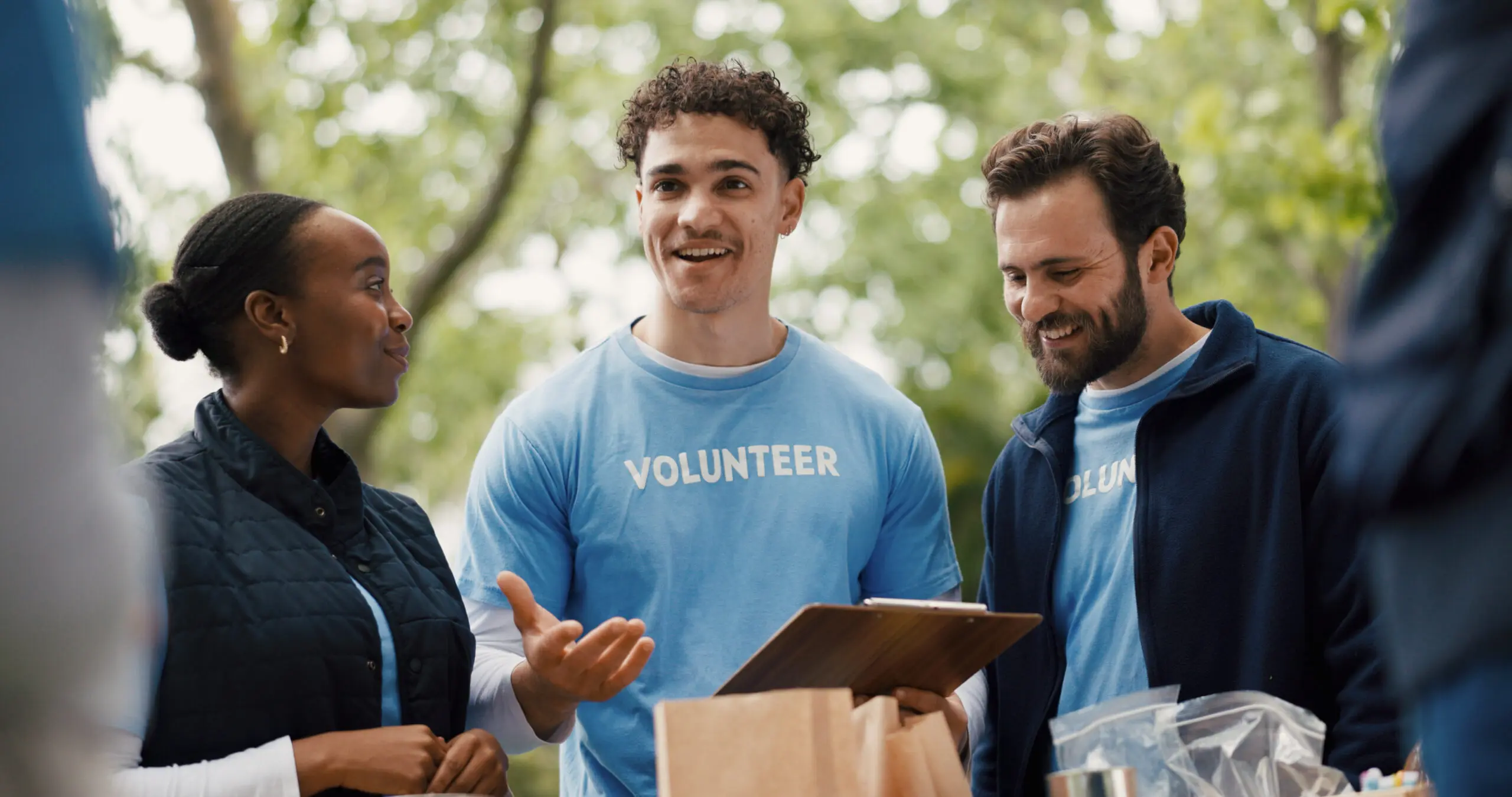 Happy people, clipboard and volunteer with team for food donation, charity or community service. Group, NGO or society with smile for global outreach, poverty or economic stability in outdoor park